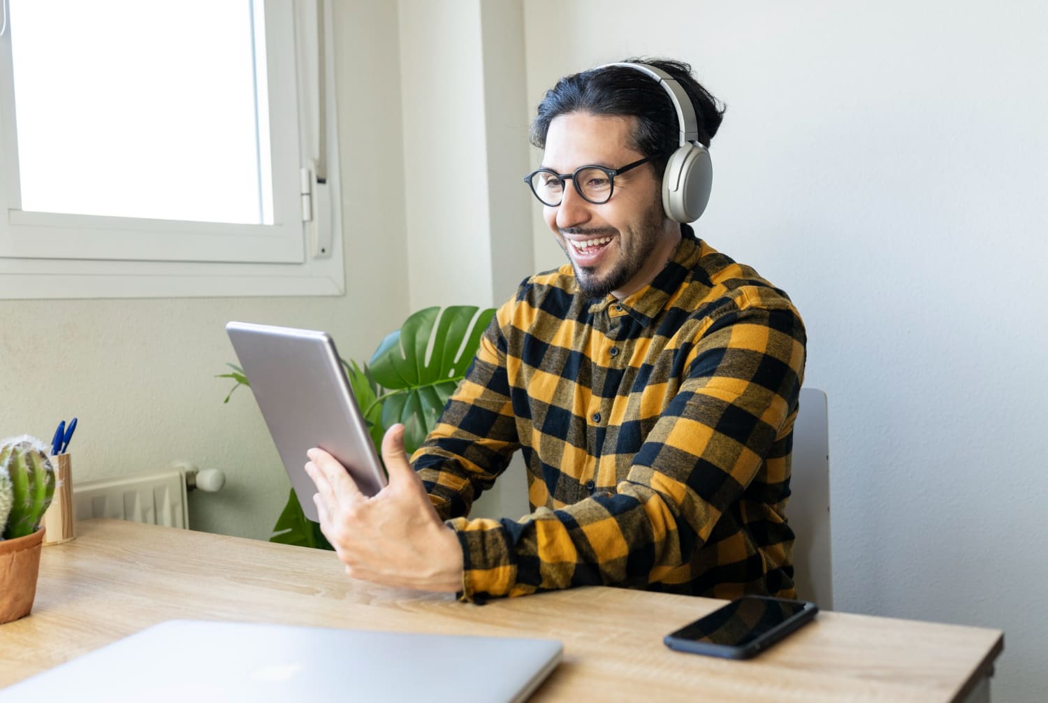Smiling man wearing headphones and using a tablet at his desk
